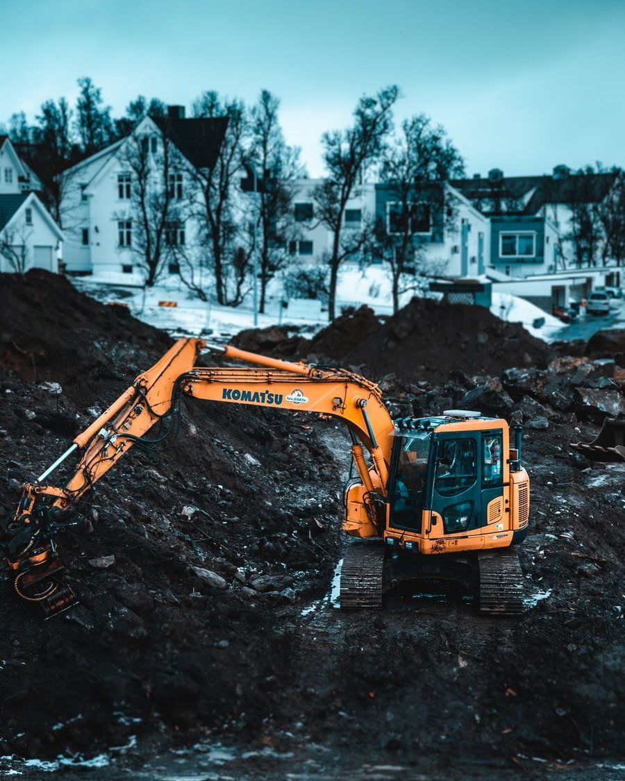 Grävmaskin i schakt framför bostadshus